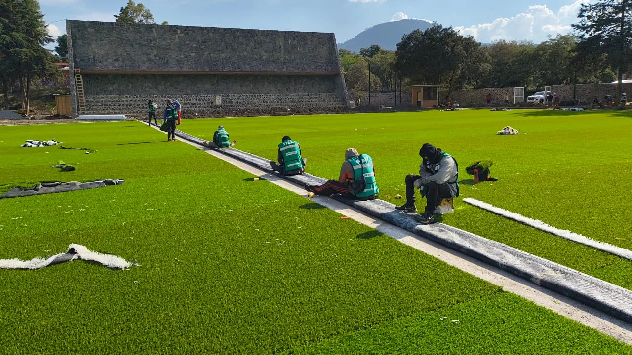 Instaladores extendiendo y tensando pasto sintético verde en una cancha de futbol