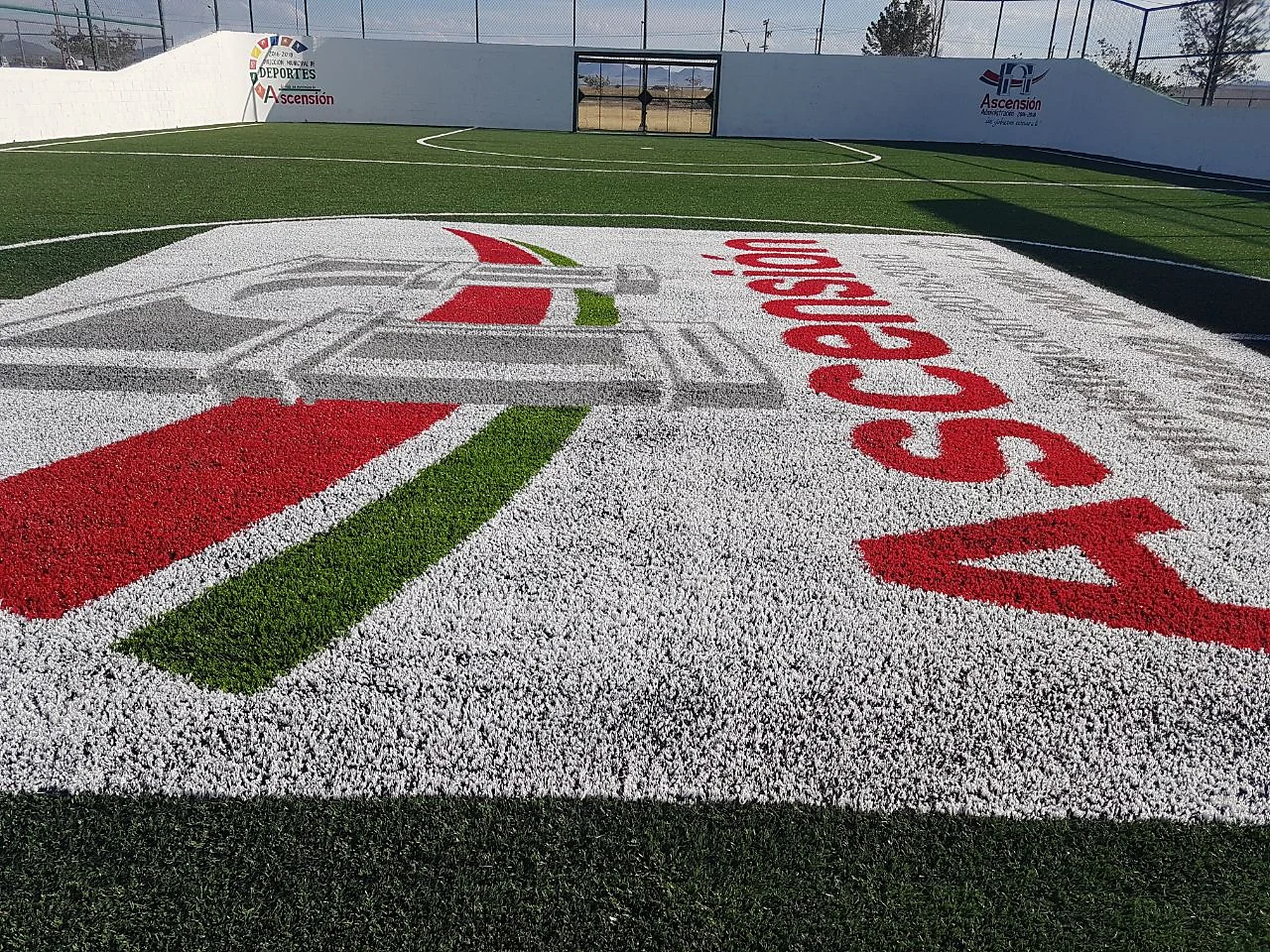 Detalle en diagonal del logotipo de Ascensión con letras rojas y franja verde cortadas en pasto sintético de color