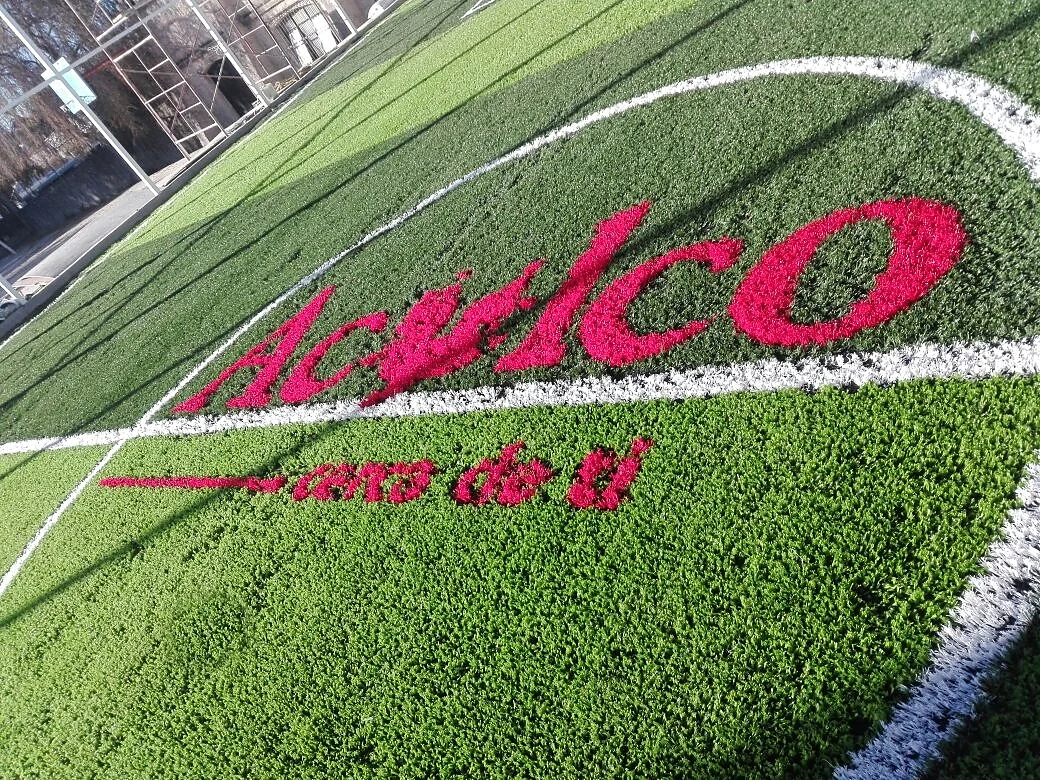 Nombre Aculco en pasto sintético rosa insertado en una cancha verde, detalle del corte de las letras
