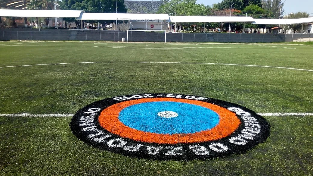 Escudo circular del Gobierno de Zapotlanejo 2015-2018 insertado en pasto sintético con la portería al fondo