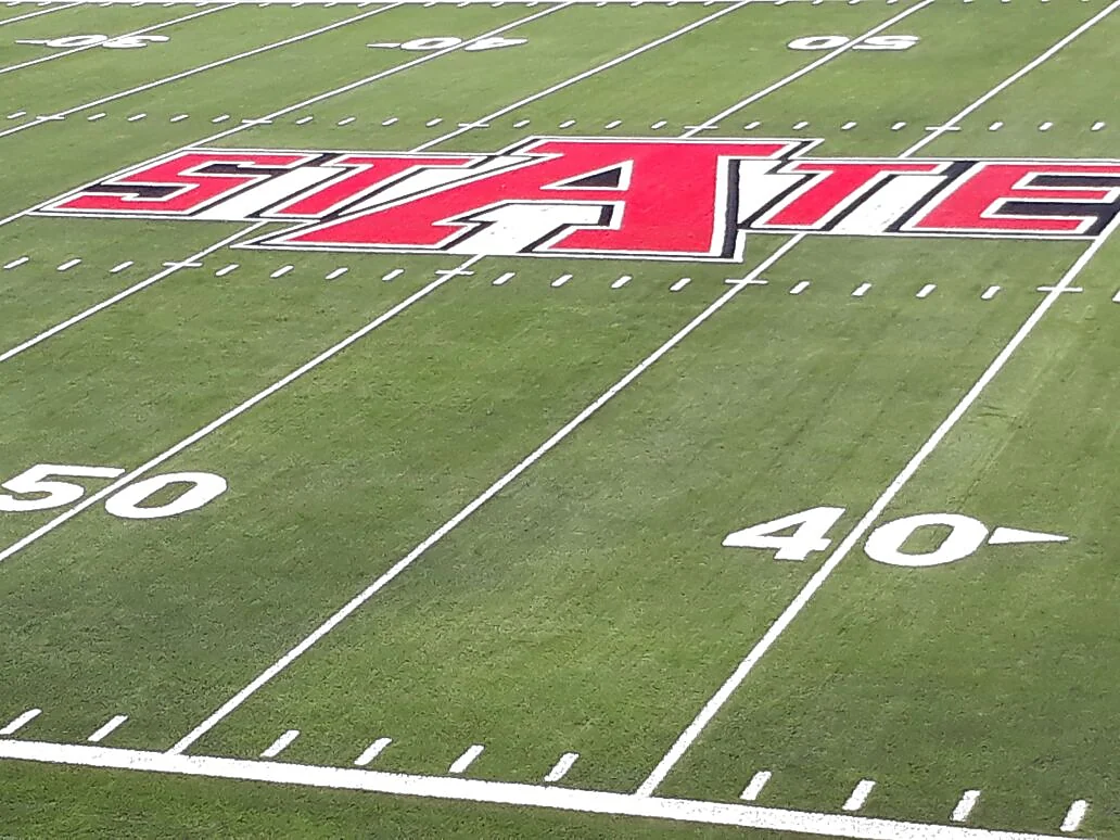Zona de anotación con la palabra STATE y las yardas 40 y 50 insertadas en pasto sintético en el campo de fútbol americano de Arkansas State University, Querétaro
