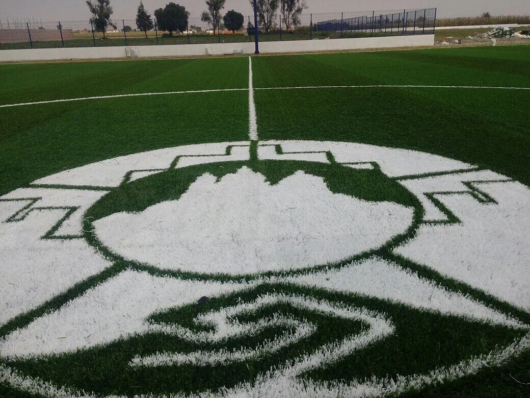Detalle cercano del corte de las figuras de un escudo blanco insertado en pasto sintético