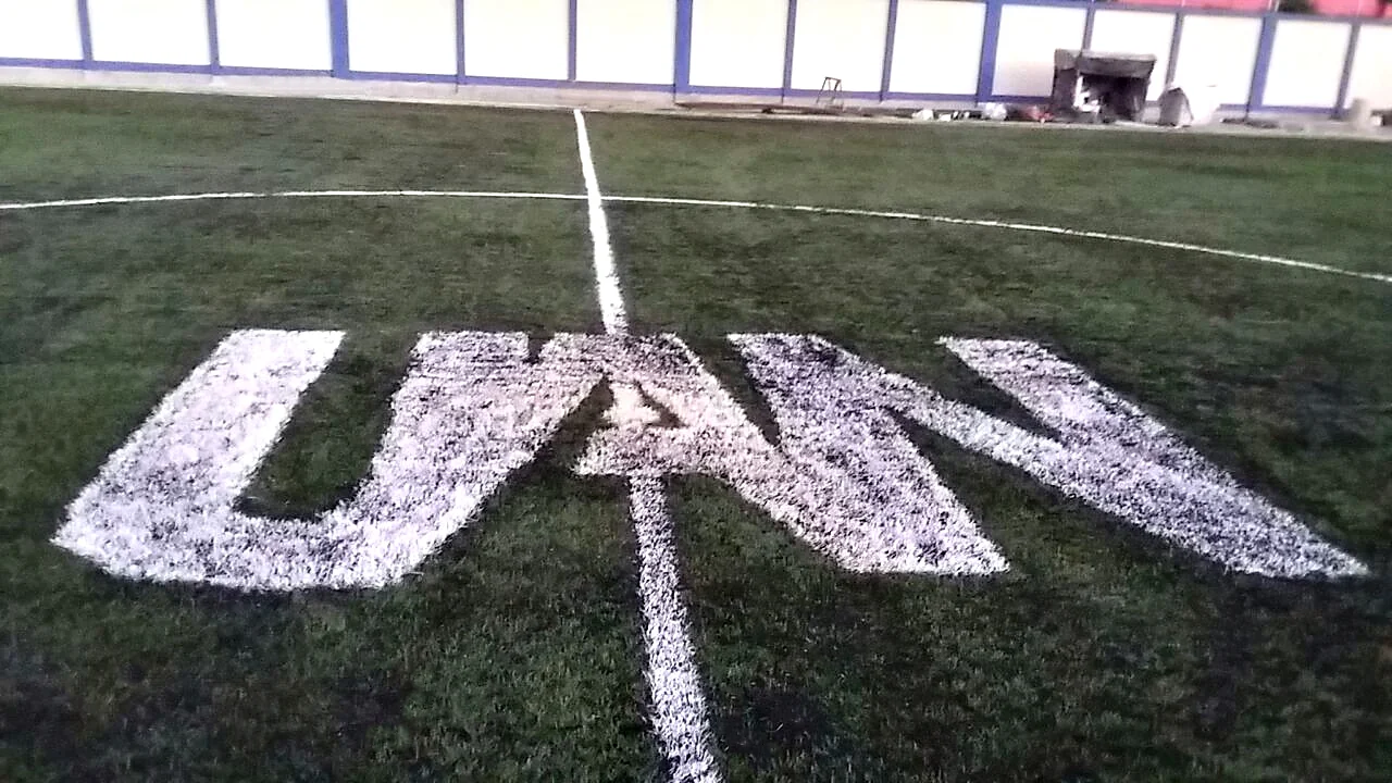 Siglas UAN insertadas en pasto sintético blanco en el círculo central de la cancha de una preparatoria en Tepic, Nayarit