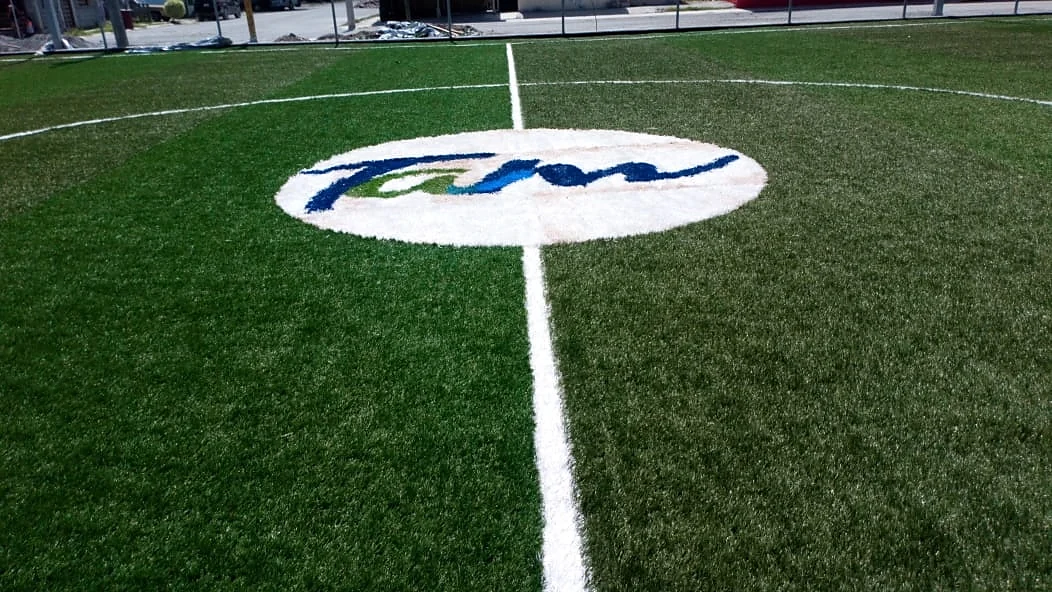 Logotipo Tam insertado en pasto sintético en el círculo central de una cancha de fútbol 7 en Reynosa, Tamaulipas