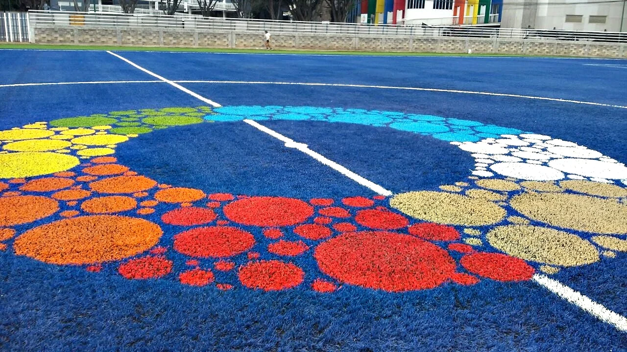 Detalle de un logotipo de círculos multicolor insertado sobre pasto sintético azul en el Deportivo Benito Juárez, Ciudad de México