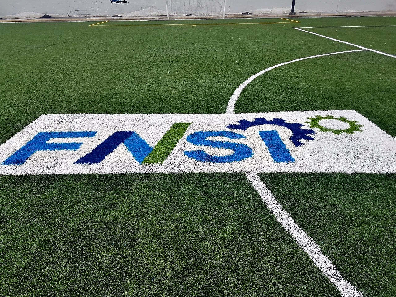Detalle cercano de las letras azul, verde y amarillo del logotipo FNSI insertadas en pasto sintético