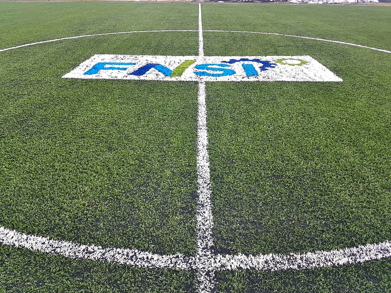 Vista general de una cancha de pasto sintético con el logotipo FNSI insertado en el círculo central