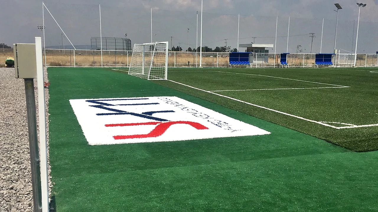 Logotipo Y-Tec Keylex México insertado en pasto sintético en una cancha de fútbol 7 de planta industrial con la portería al fondo