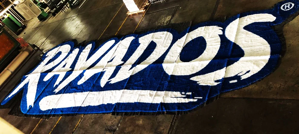 Logotipo Rayados en azul y blanco armado en pasto sintético sobre piso de taller, pieza por pieza