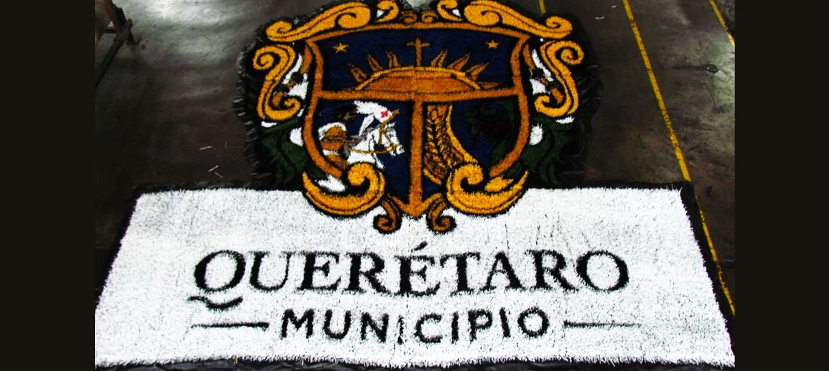 Escudo del Municipio de Querétaro con la leyenda Querétaro Municipio armado en pasto sintético blanco, negro y dorado sobre piso de taller
