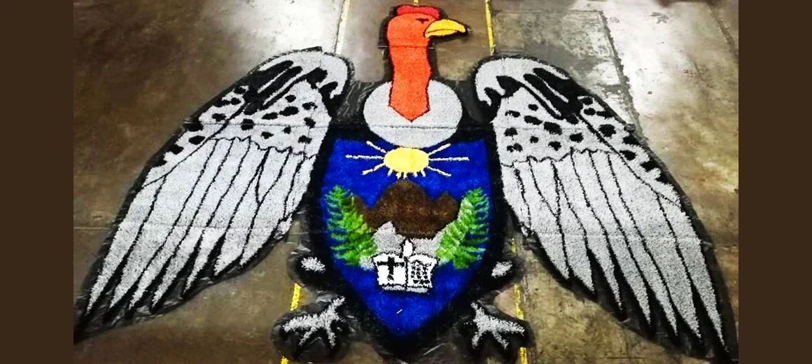 Escudo con águila de alas abiertas en blanco, negro, azul y verde armado en pasto sintético sobre piso de taller