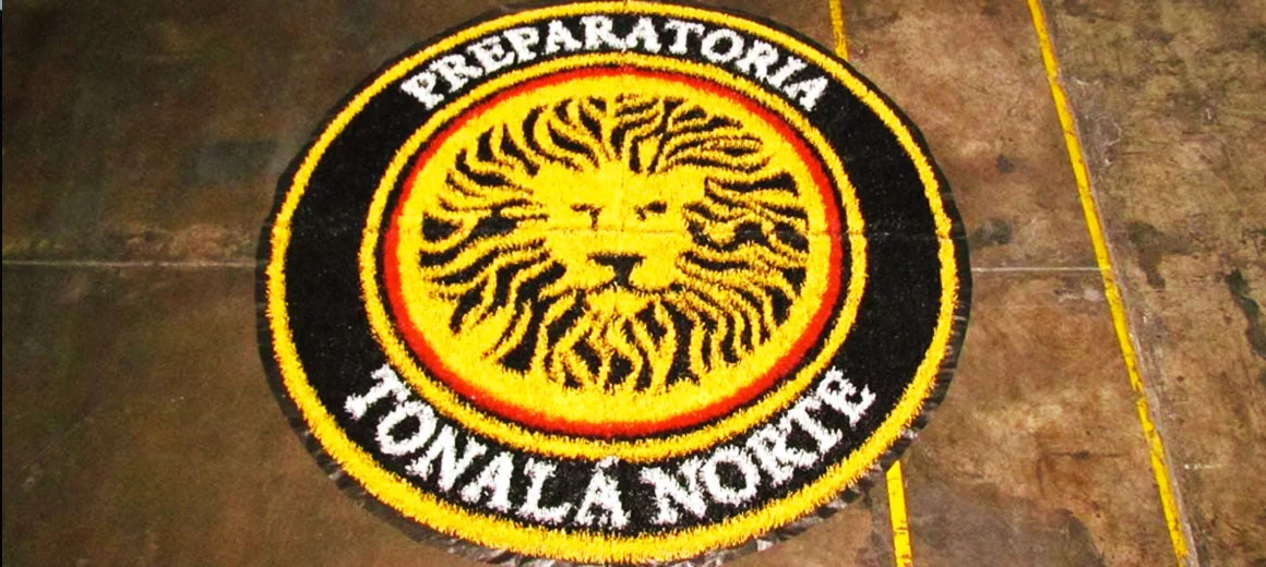 Escudo circular de la Preparatoria Tonalá Norte con un león sobre fondo amarillo, rojo y negro armado en pasto sintético en taller