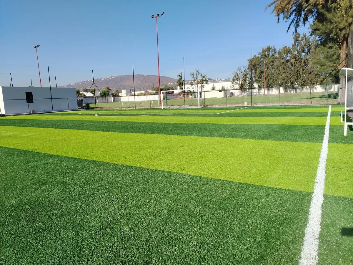 Cancha de fútbol 7 con pasto sintético a franjas y malla perimetral en el Club Atlético Balam, Zapopan, con cerros al fondo