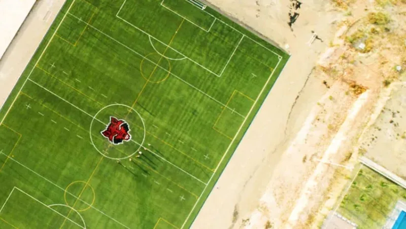 Cancha de soccer con pasto sintético y escudo en el círculo central en Arkansas State University, campus Querétaro, vista aérea