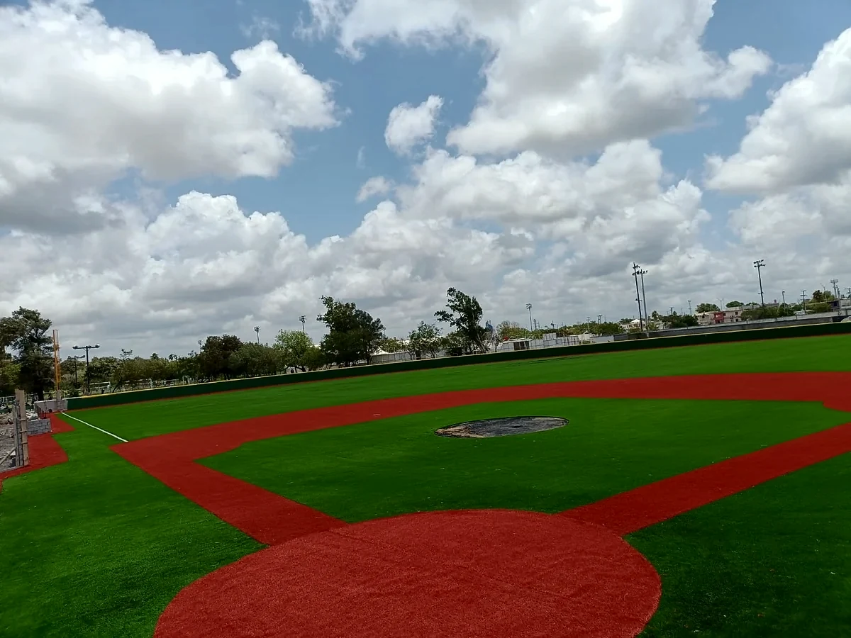 Cuadro del campo de béisbol con pasto sintético verde y terracota y barda verde del jardín en Matamoros