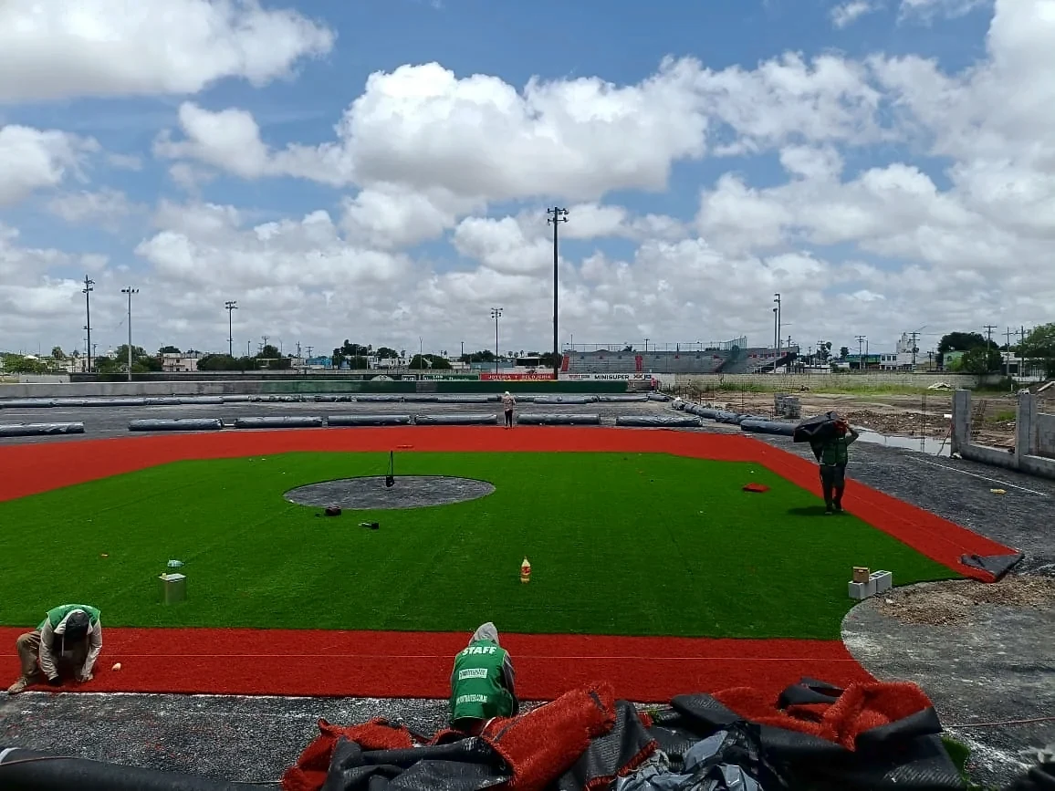 Equipo de Sportmaster instalando el pasto sintético terracota del cuadro del campo de béisbol en Matamoros, Tamaulipas